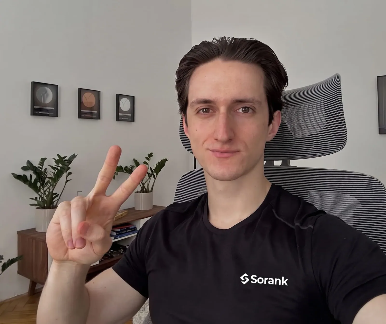 Hombre con camiseta negra de Sorank sentado en una silla de oficina haciendo el signo de la paz
