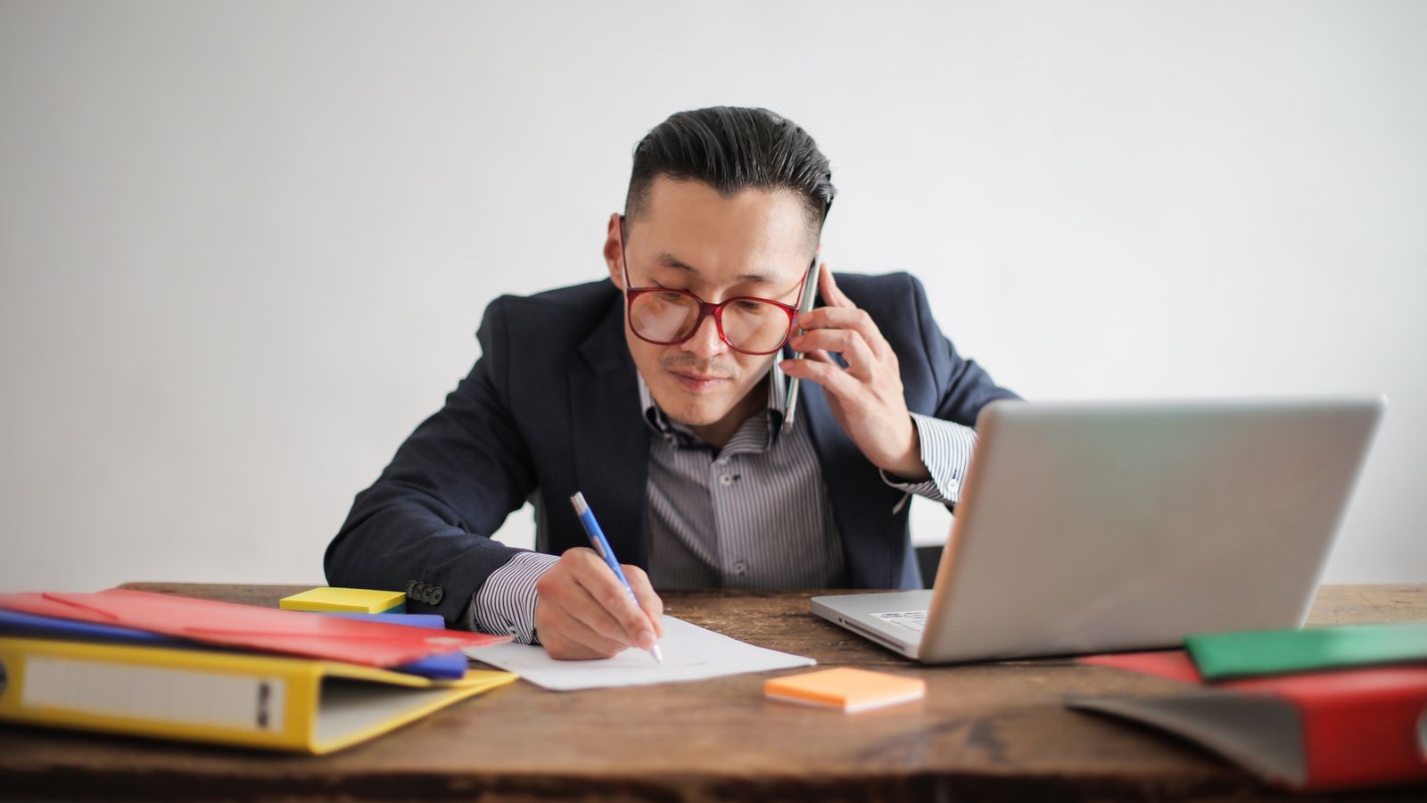 ノートパソコンとメモを置いた机で、B2Bの営業電話をかけている営業担当者
