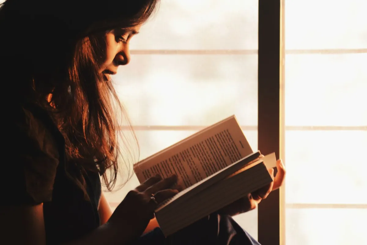 Woman reading a book by a sunlit window