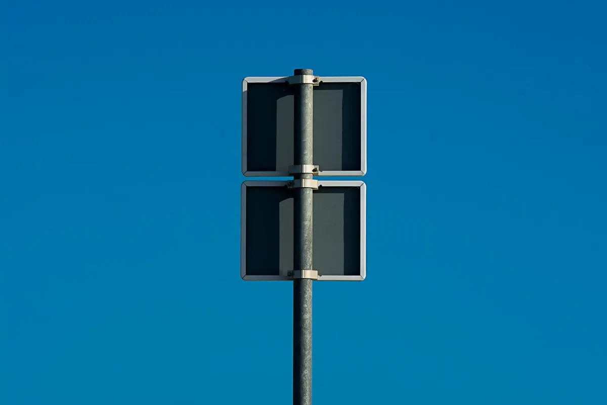 Two blank street signs on a pole against a clear blue sky