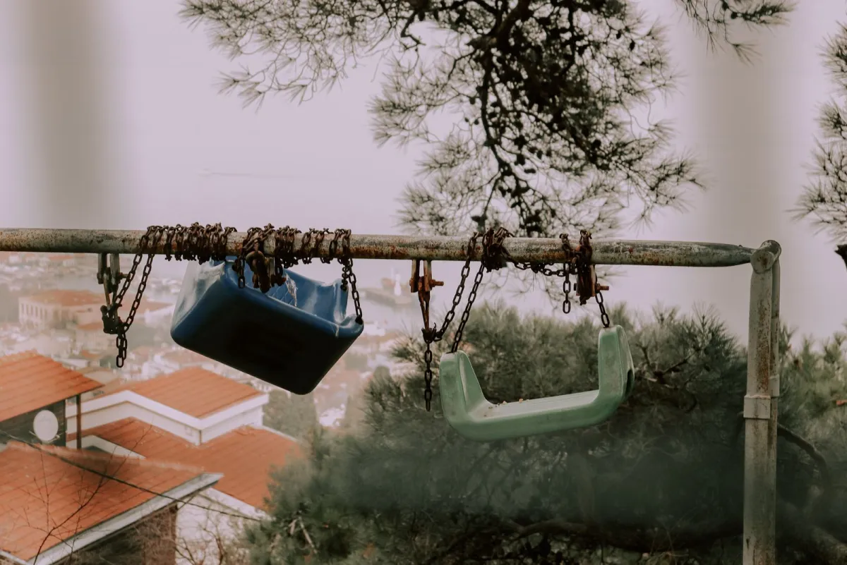 Old playground swings hanging from broken, rusty chains