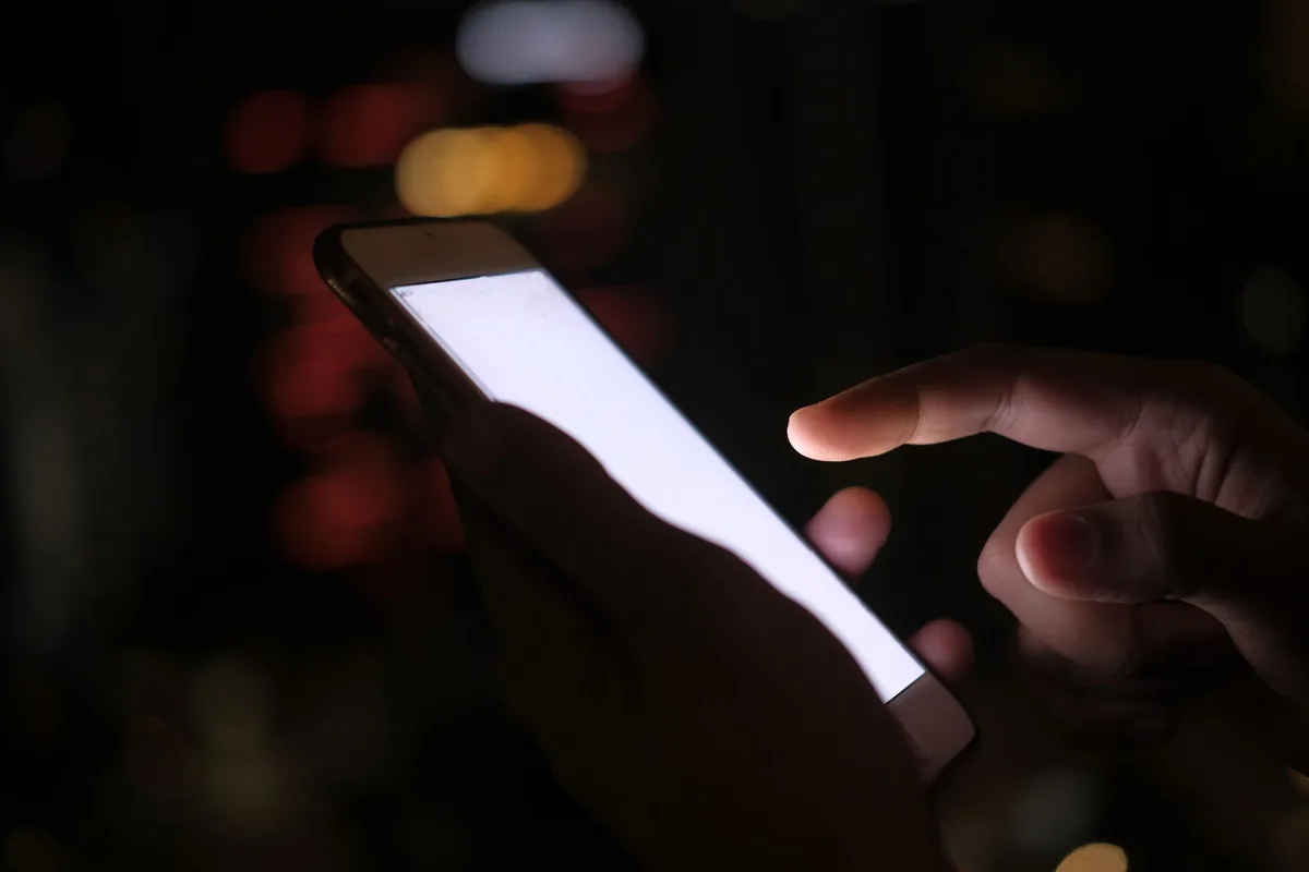 Hand using a glowing smartphone at night with blurred city lights behind