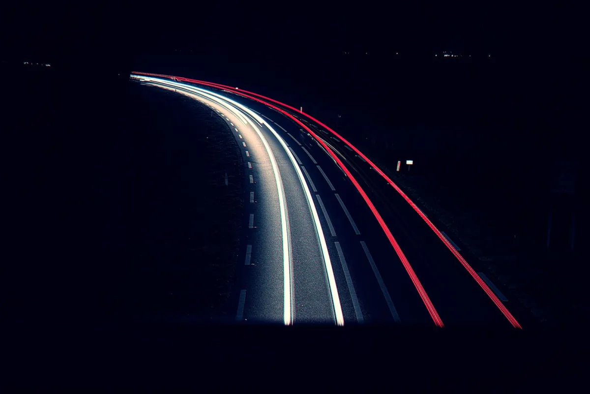 White and red car light trails on a curving road at night