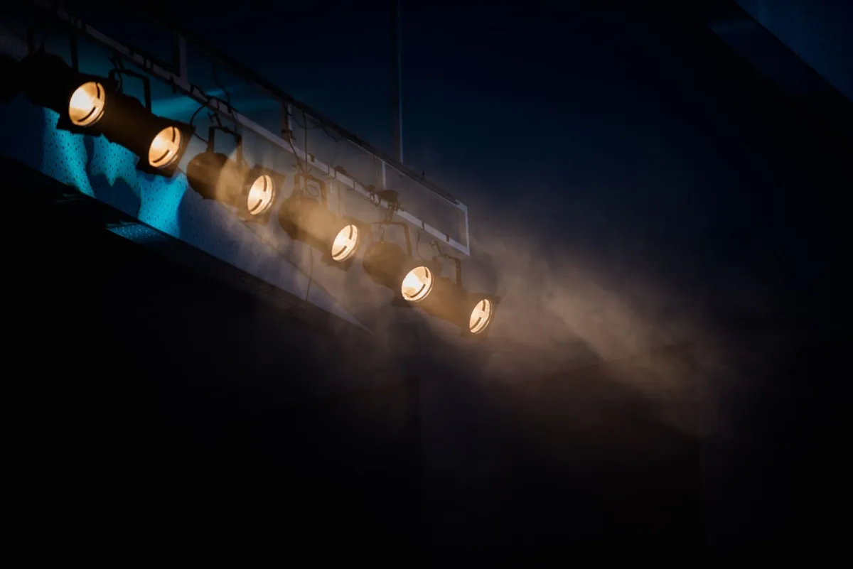 Row of stage spotlights shining through haze in a dark theater
