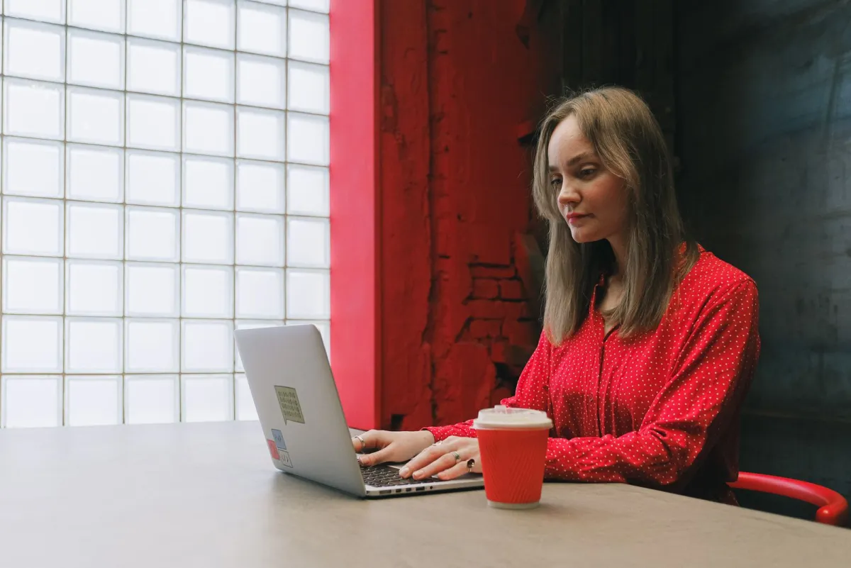 Woman in a red blouse working on a laptop next to a glass block wall