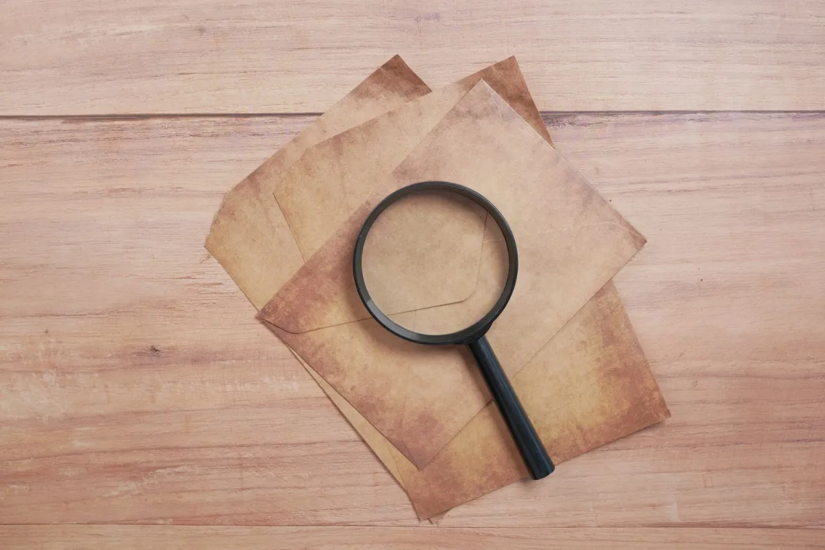 Black magnifying glass resting on blank aged paper on a wooden table