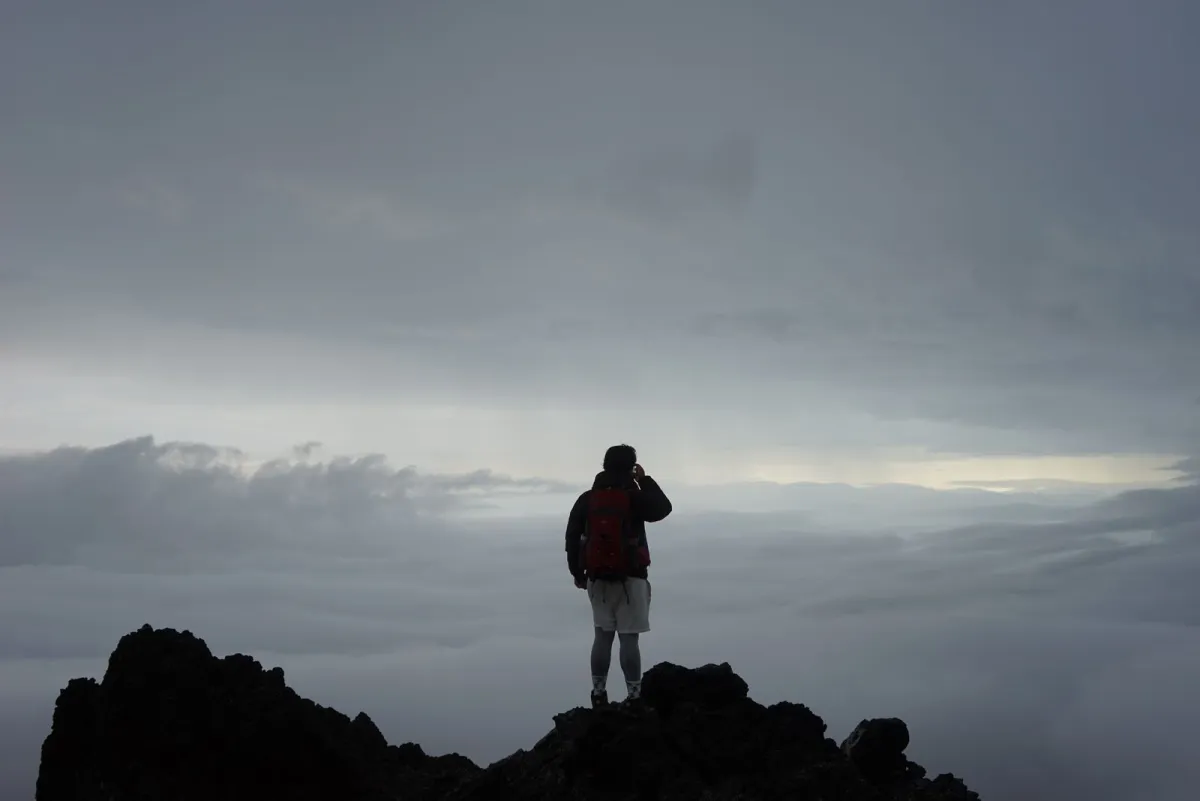 Hiker standing on a rocky summit above the clouds