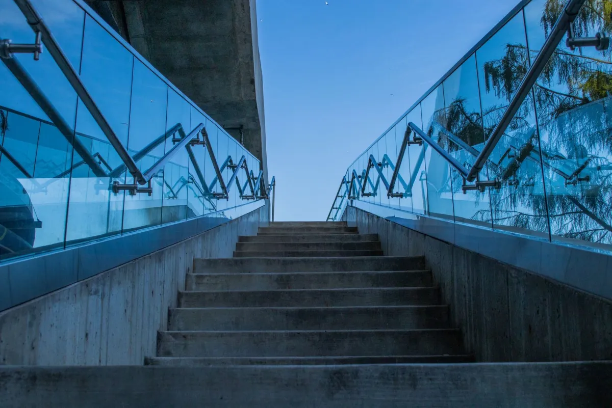 Concrete stairs rising between glass railings toward a blue sky