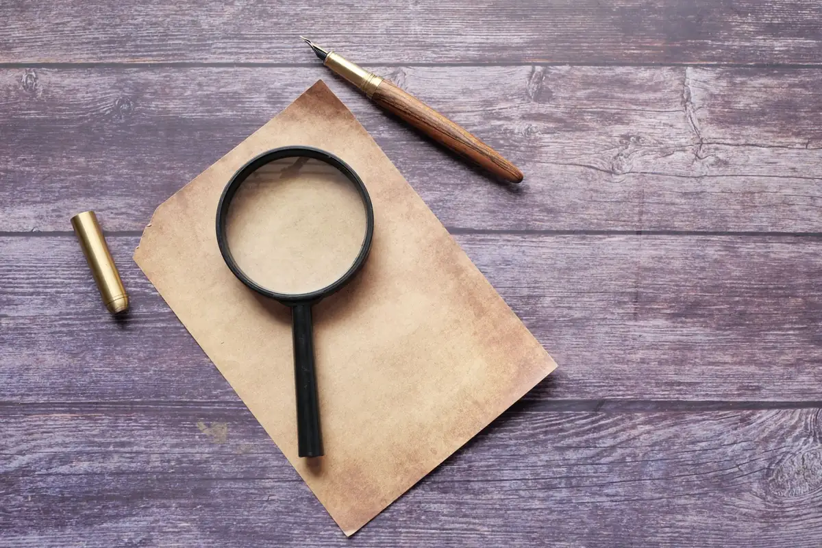 Magnifying glass and fountain pen on an old sheet of paper on a wooden table