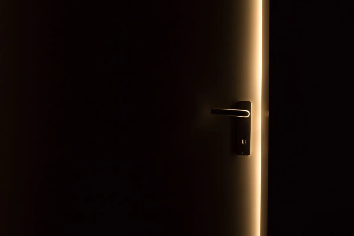 Pintu yang dibiarkan sedikit terbuka di ruangan gelap dengan seberkas cahaya yang masuk