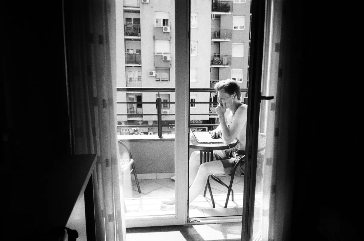 Man working on a laptop on a sunny city balcony, in black and white