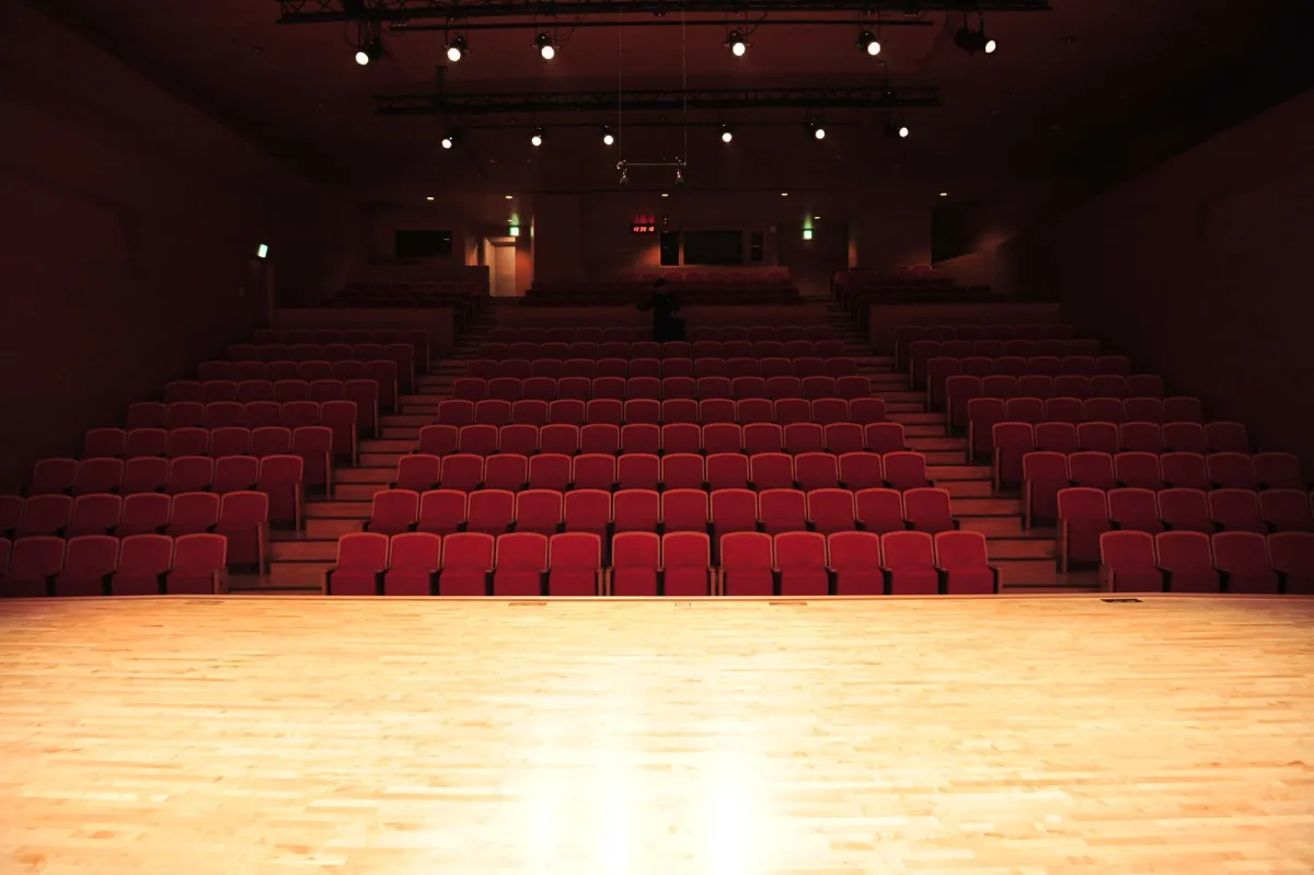 Teater kosong dengan deretan kursi merah yang terlihat dari panggung kayu yang terang