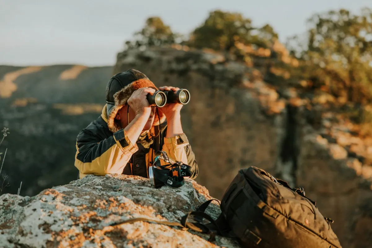 Hiker on a rock scanning the landscape with binoculars