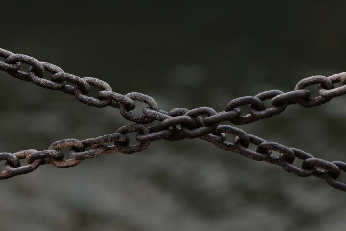 Two rusty metal chains crossing against a dark background