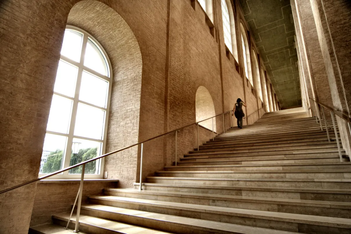 Person climbing a long staircase in a bright stone hall
