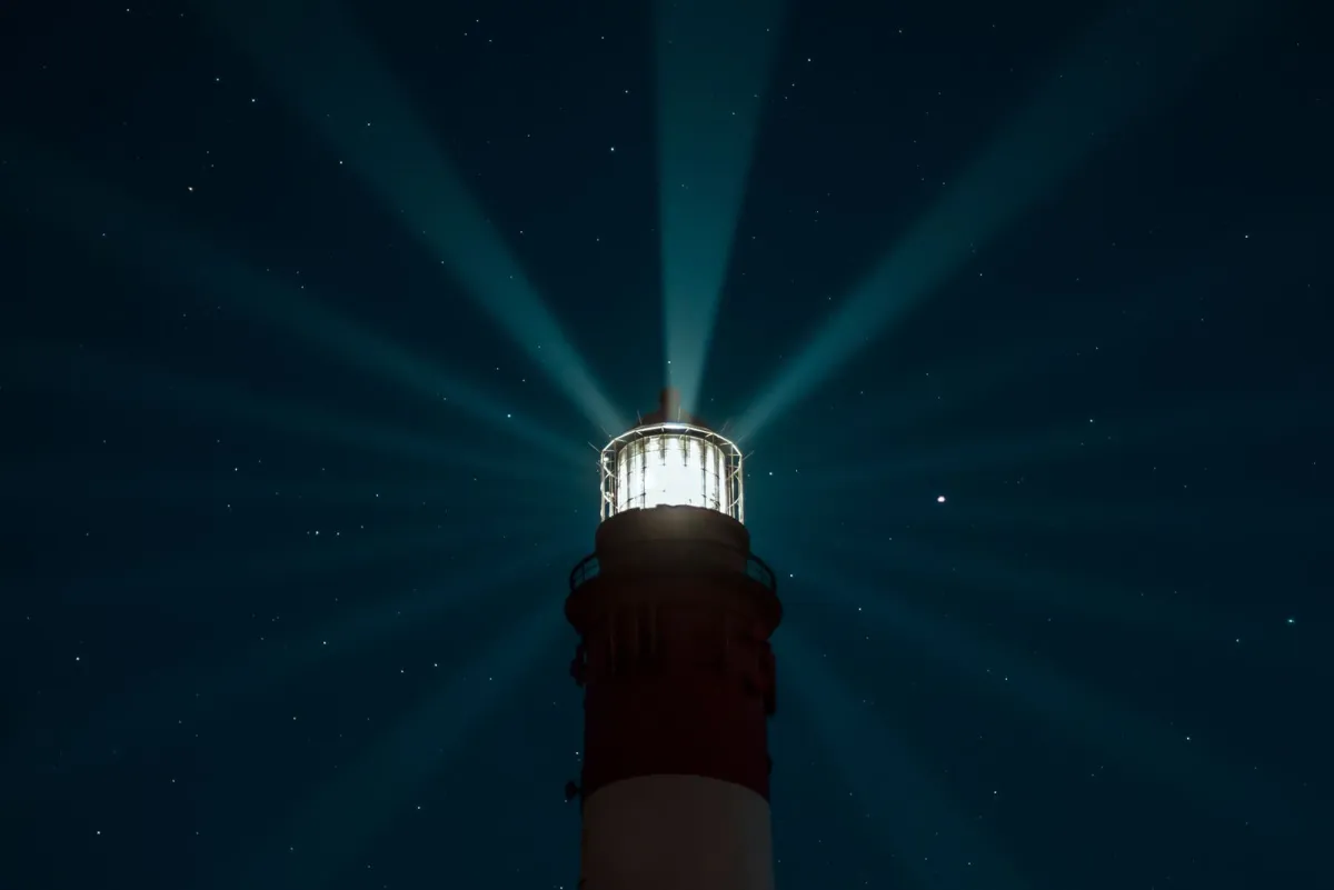 Lighthouse sending beams of light across a starry night sky