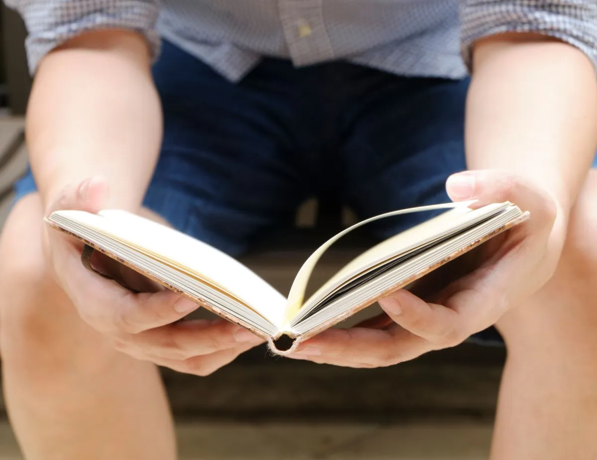 Man holding an open book on his knees