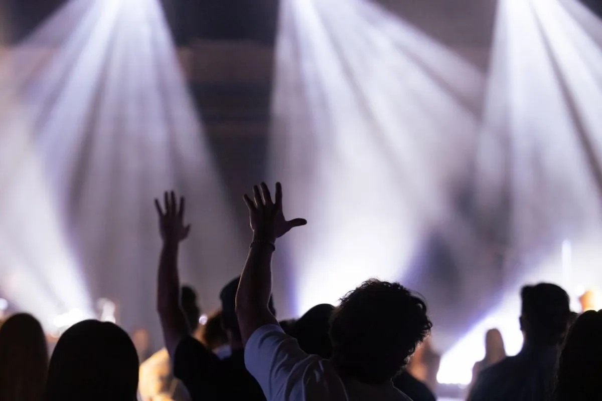 Crowd raising their hands in front of a stage lit by white spotlights