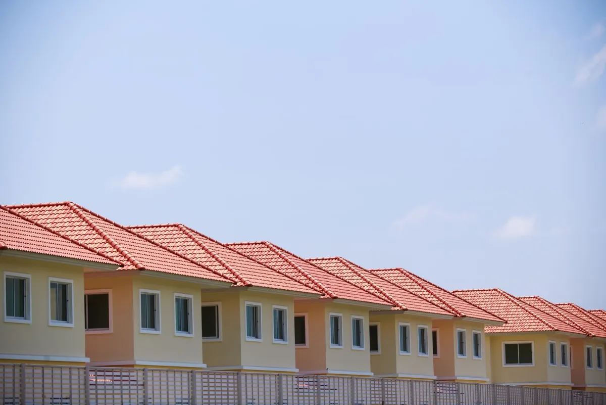 Line of identical suburban houses with red roofs under a blue sky