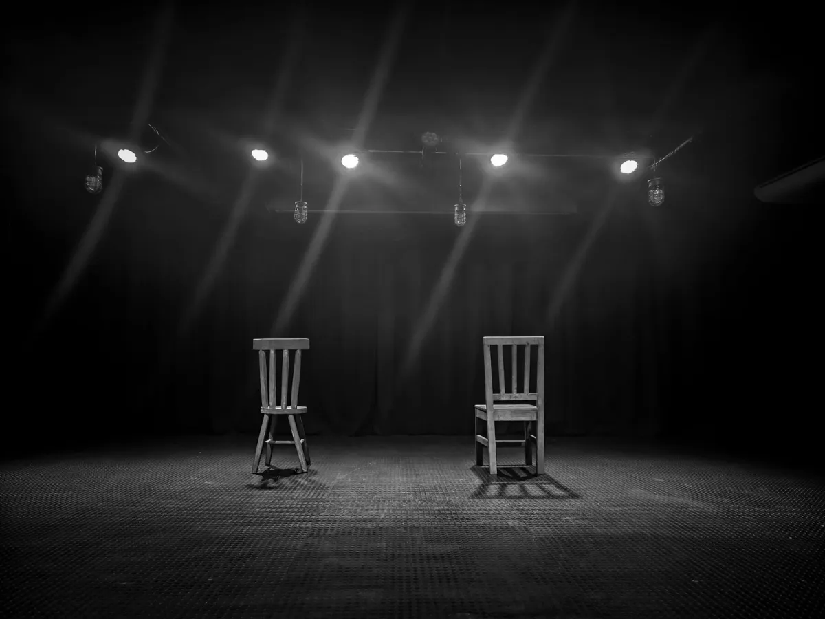 Two empty chairs under spotlights on a dark stage