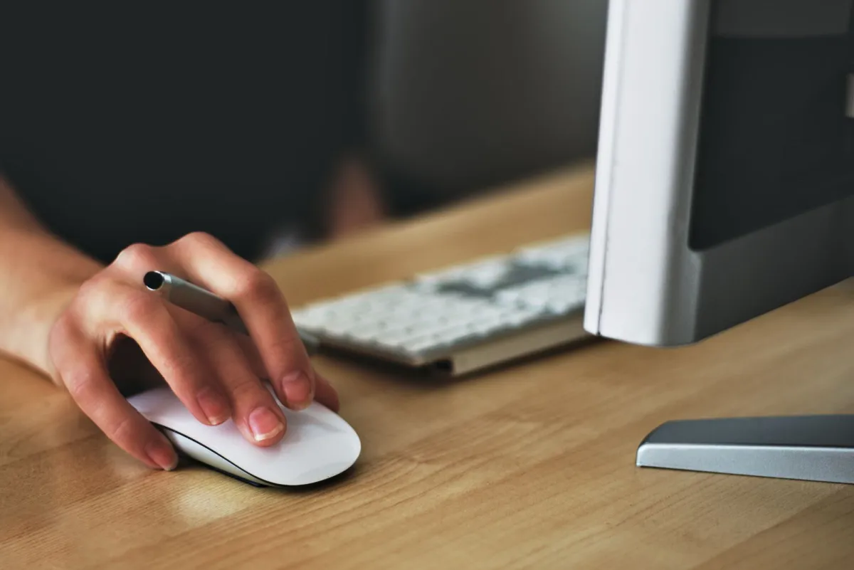 Hand using a white computer mouse on a wooden desk