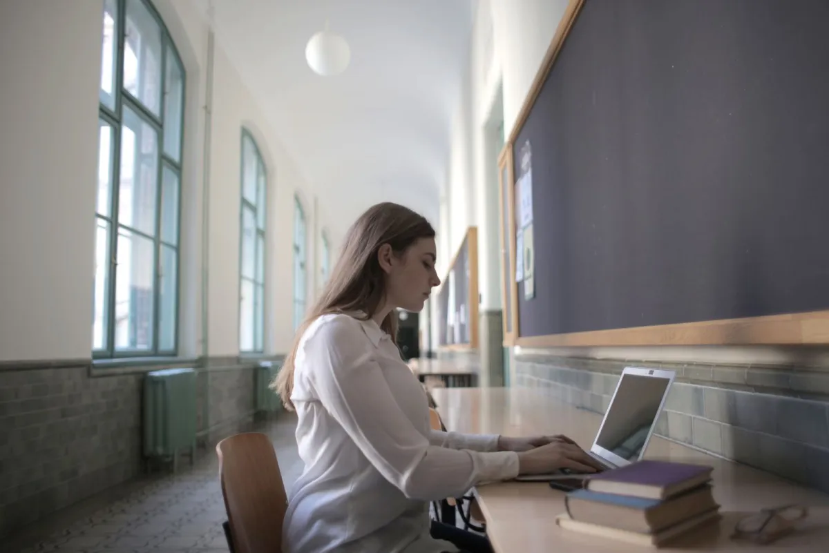 Kobieta szuka informacji na laptopie przy stole, obok niej leżą książki