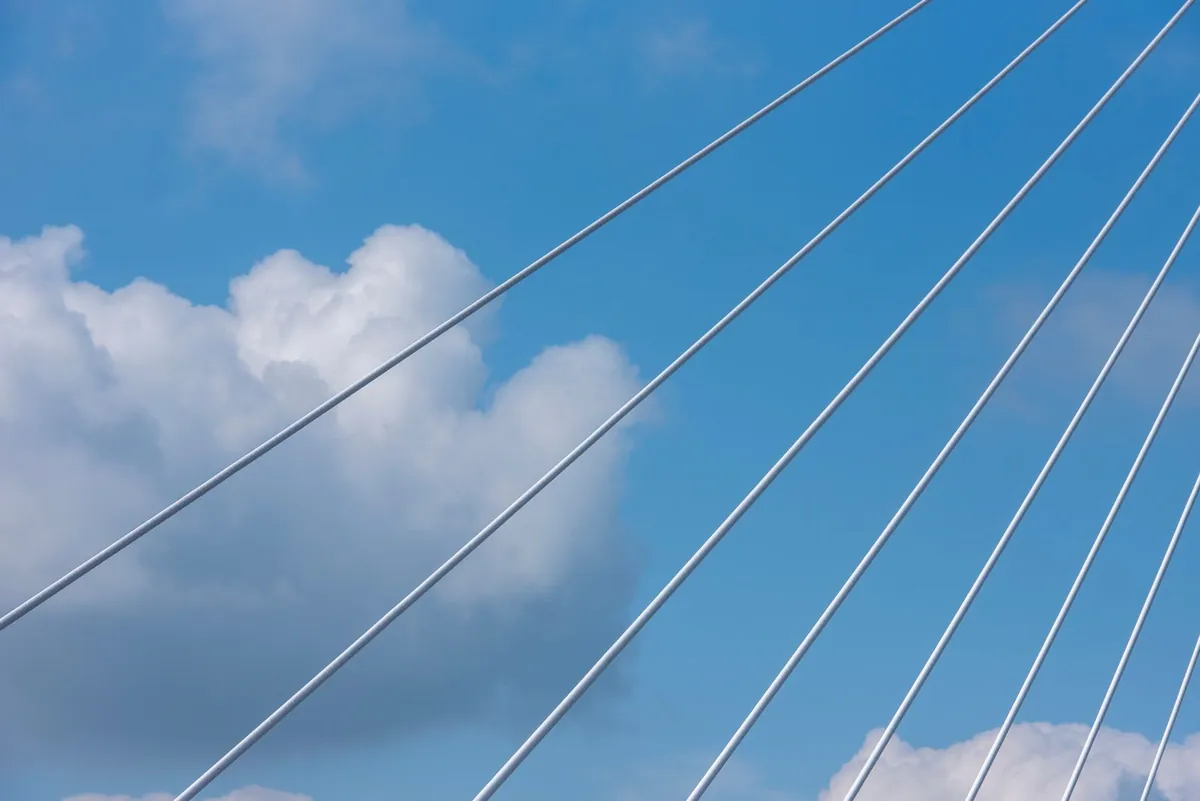 Bridge cables stretching across a blue sky with white clouds