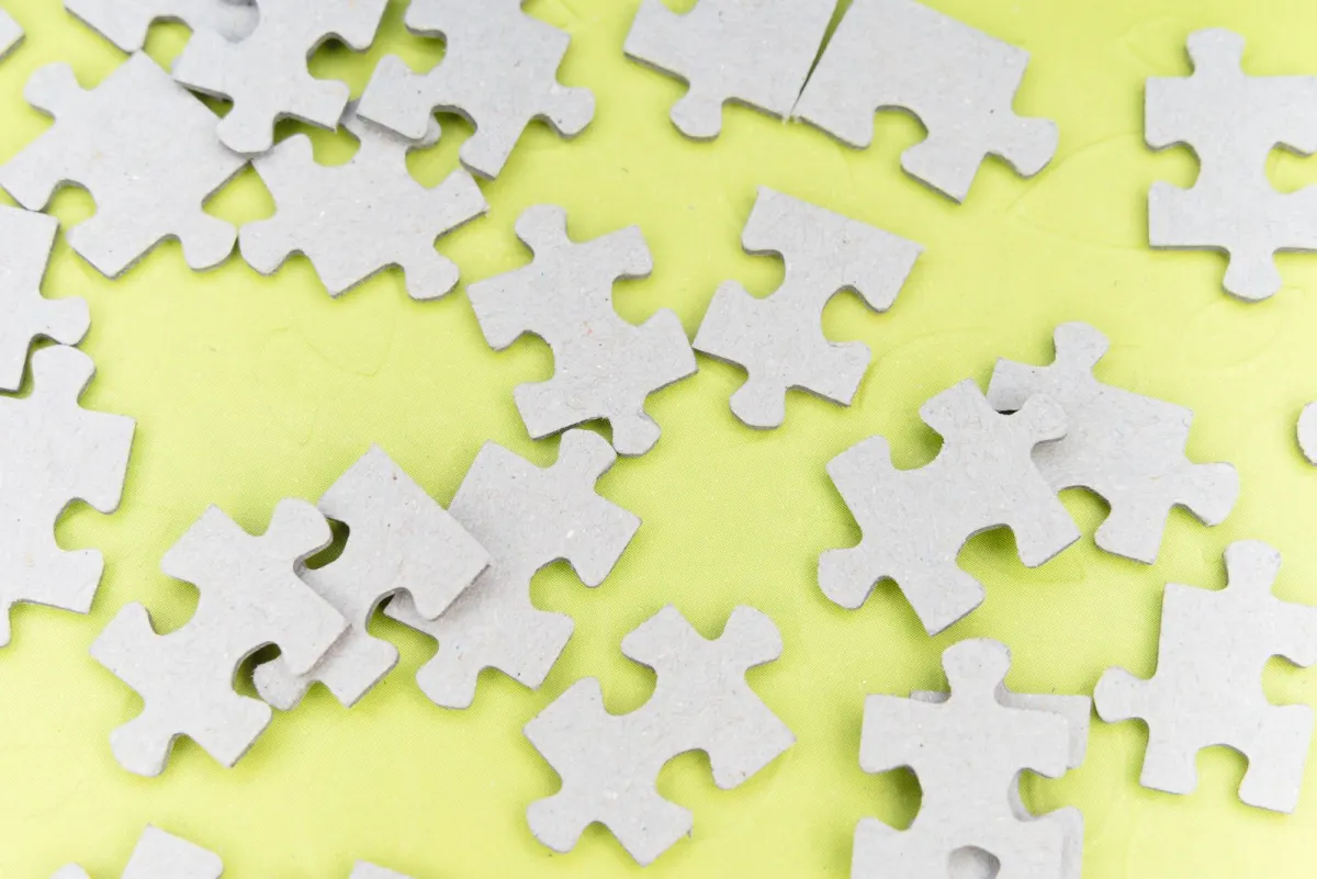 Kepingan puzzle abu-abu berserakan di atas latar kuning cerah
