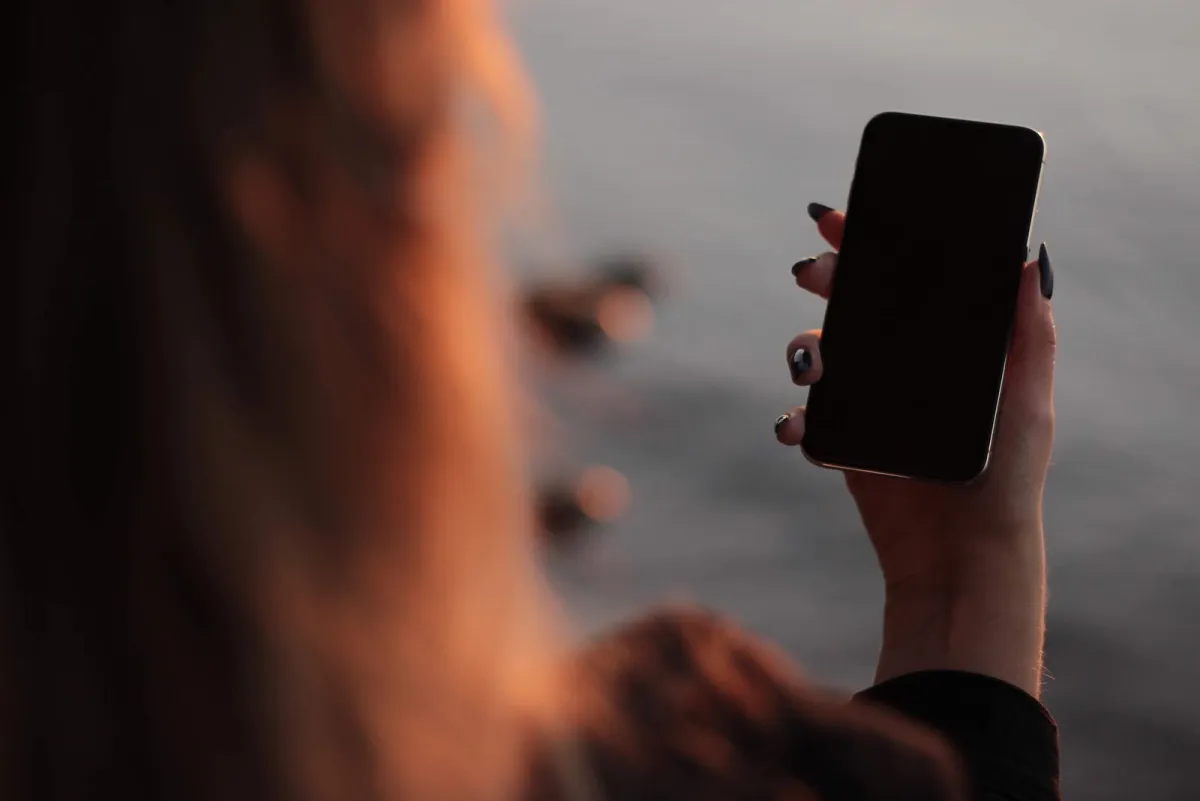 Woman holding a smartphone in front of the sea at sunset