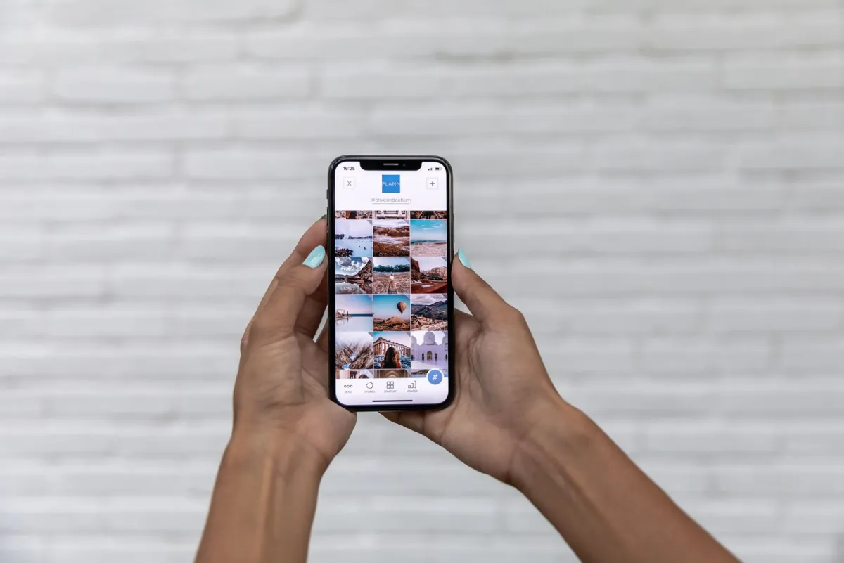 Two hands holding a smartphone in front of a white brick wall