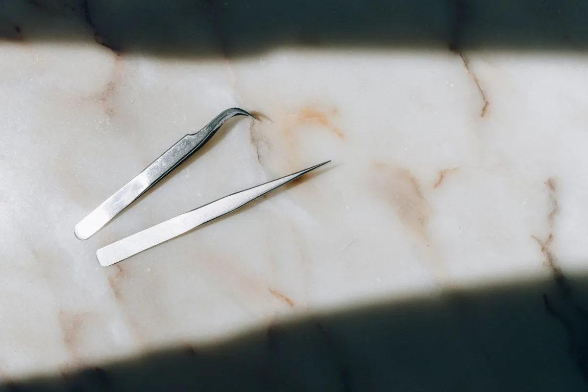 Two precision tweezers lying on a white marble surface