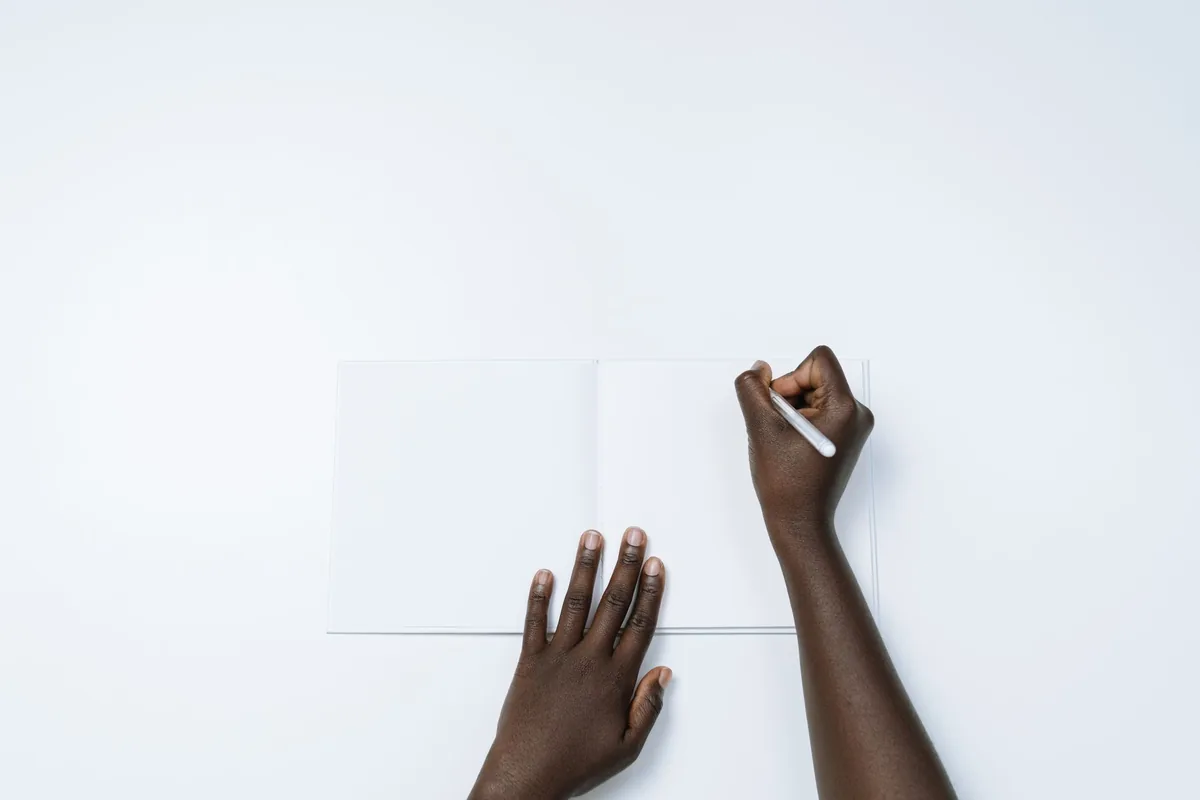 Hands about to write on the blank pages of an open notebook on a white desk