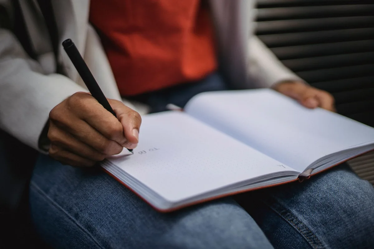 Person writing in an open notebook resting on their lap
