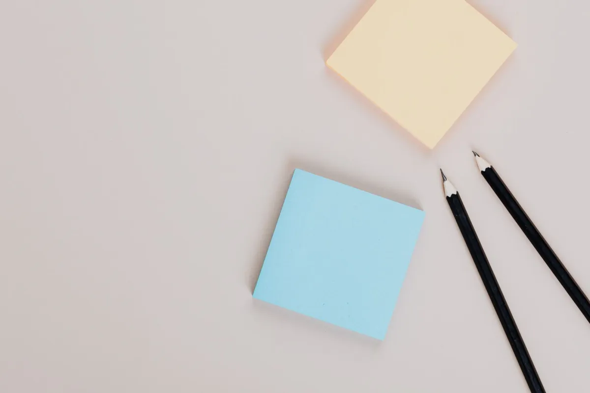 Blank sticky notes and two sharpened pencils on a pale desk
