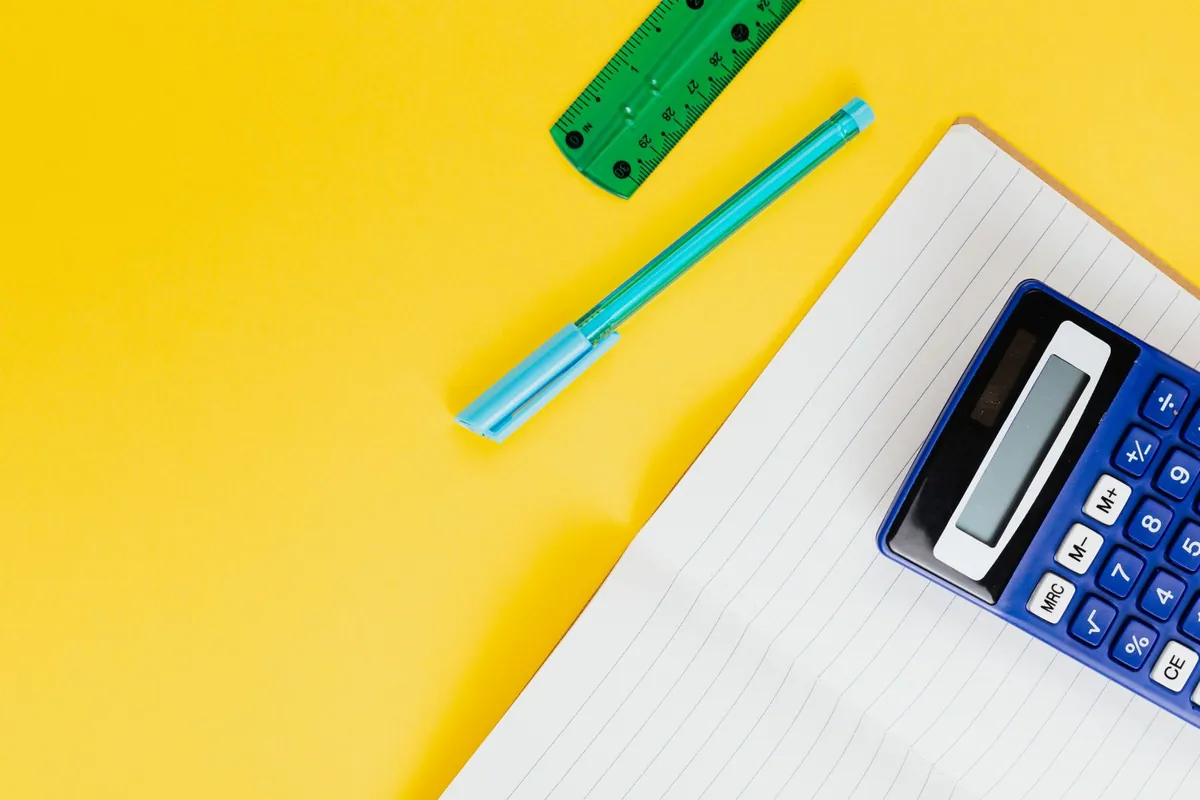 Blue calculator, notebook, pen and ruler on a yellow background