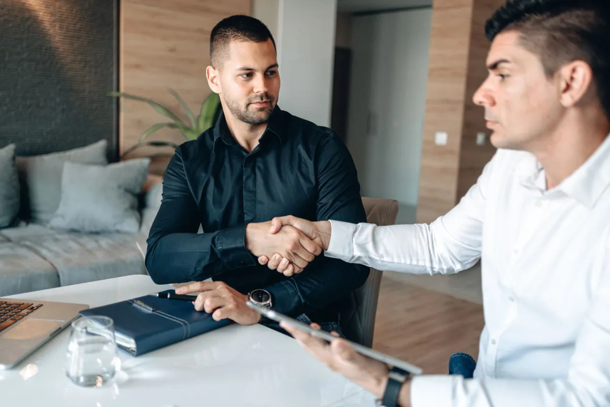 Two men shaking hands across a desk after a meeting