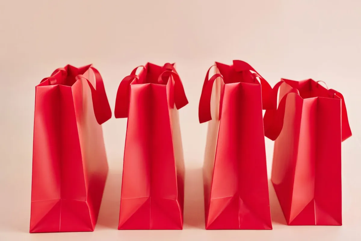 Four red paper gift bags standing in a row on a pink background