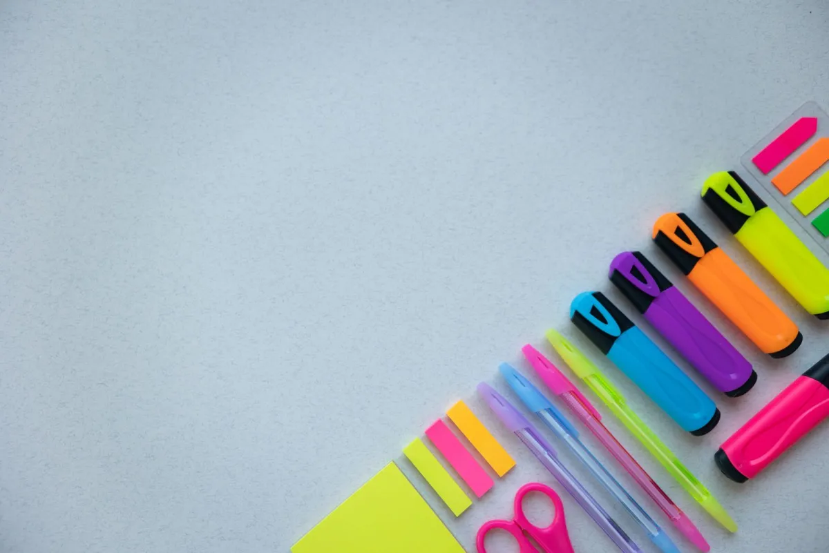 Row of colorful highlighters and pens on a light gray desk