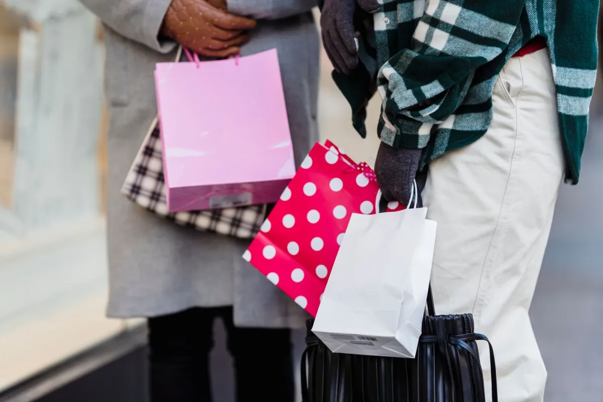 Two shoppers carrying pink, white and polka dot paper bags on a sidewalk