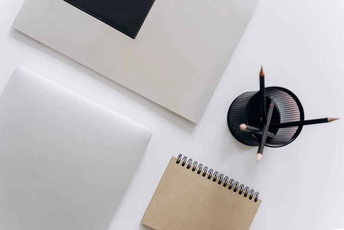 Laptop, notitieblok en potloden die op een wit bureau zijn neergelegd voordat het schrijven begint