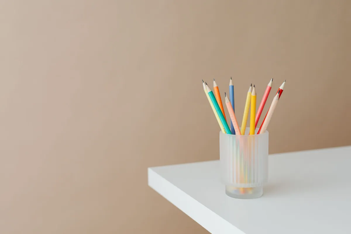 Colored pencils in a frosted glass holder on the corner of a white table