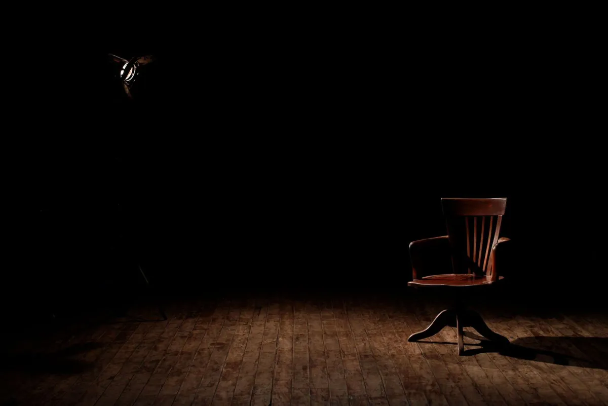 A single wooden chair lit by a spotlight on a dark stage
