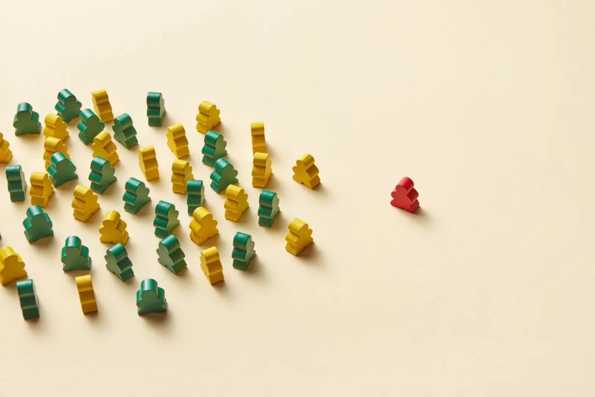 Green and yellow wooden figures gathered in groups, with one red figure apart