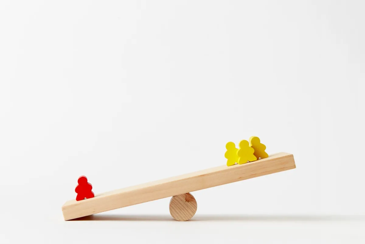 Wooden seesaw tipping under the weight of small coloured figures
