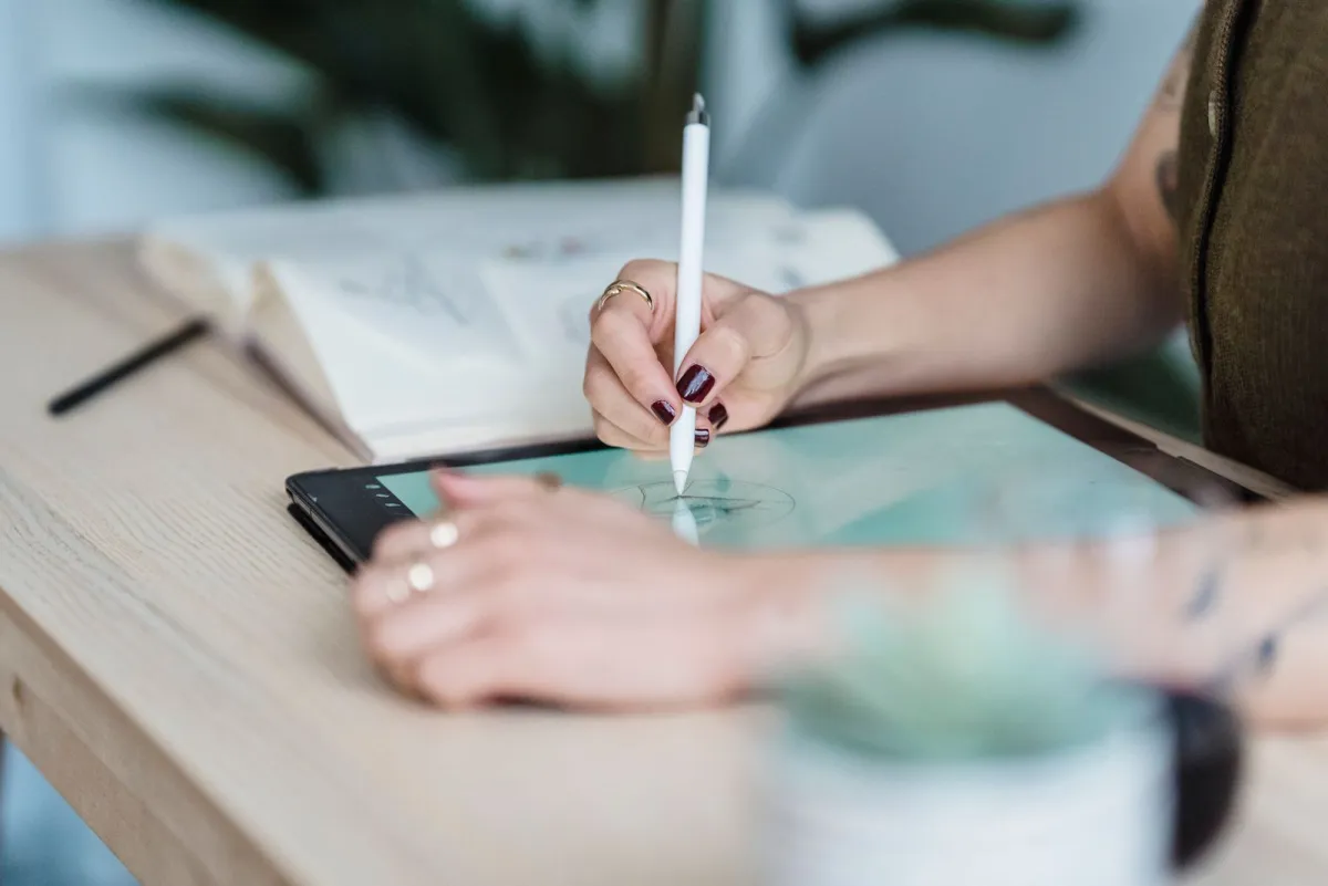 Designer drawing a small logo sketch on a tablet with a stylus at a wooden desk