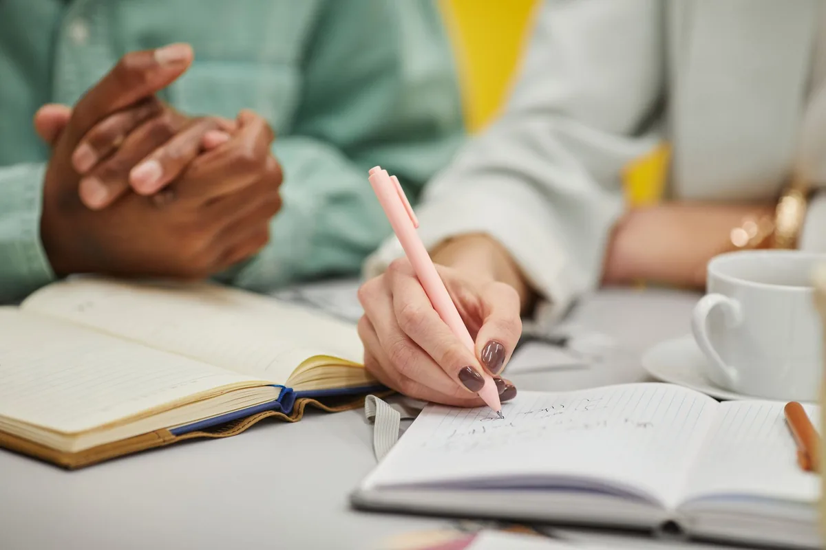 Two people taking notes in notebooks during a work meeting