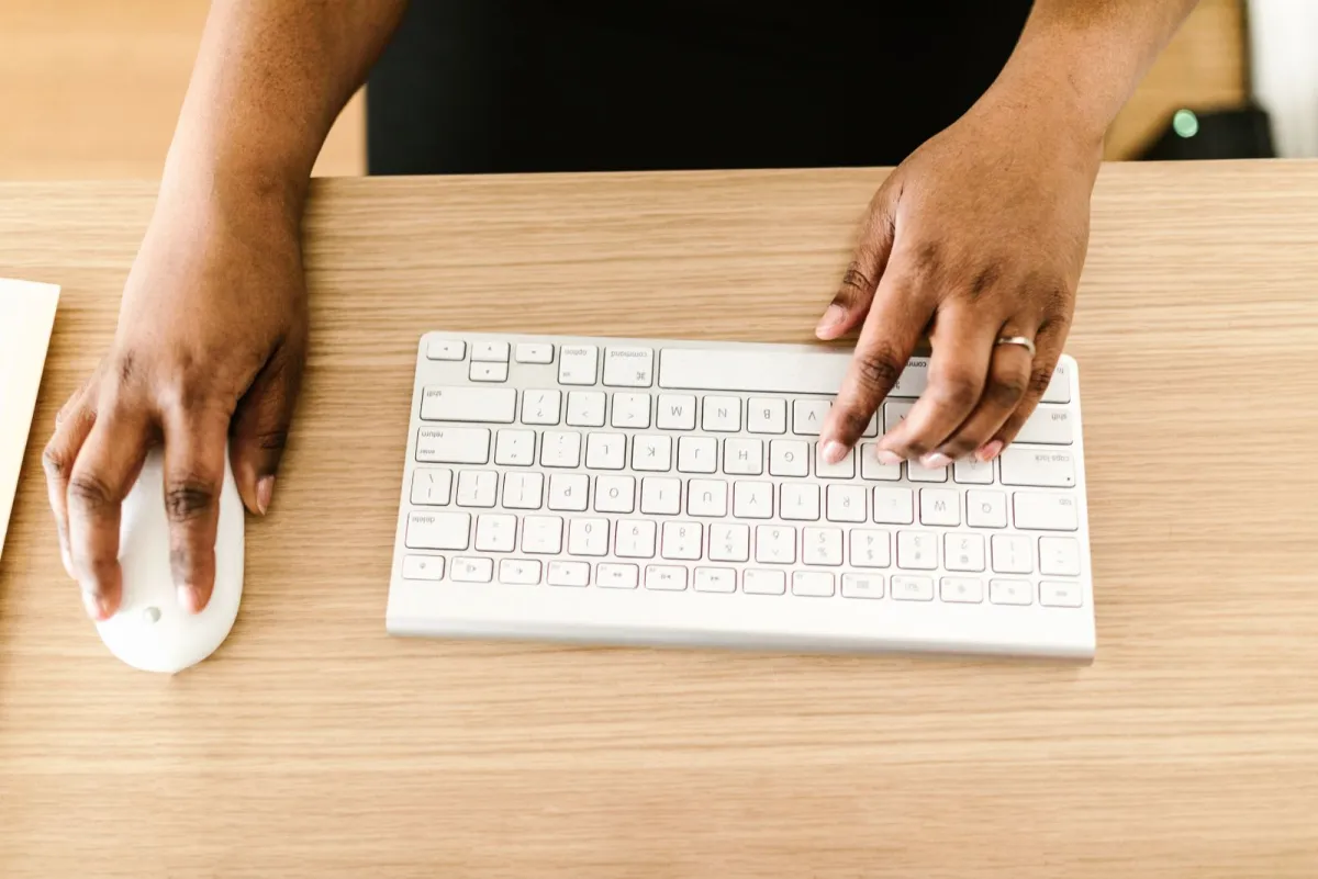 Tangan mengetik di keyboard putih di atas meja kayu