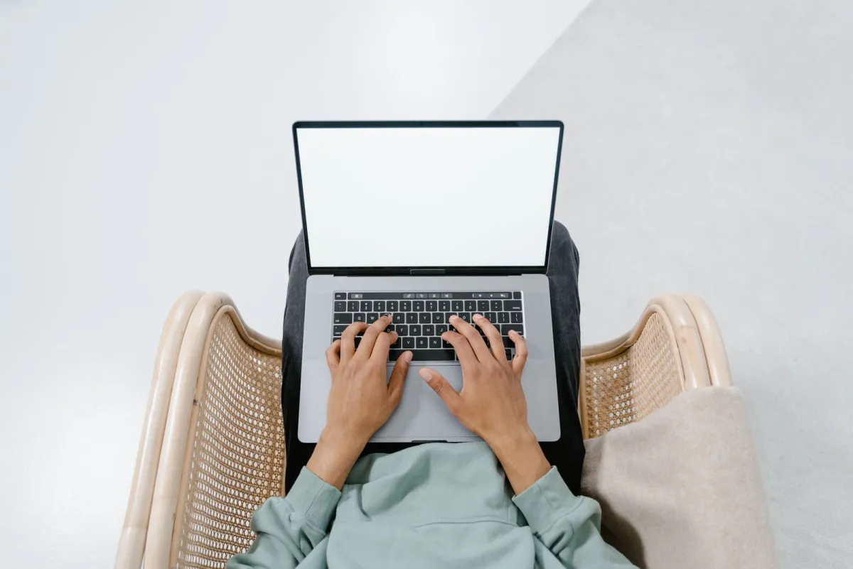 Osoba pisząca na laptopie trzymanym na kolanach, widziana z góry