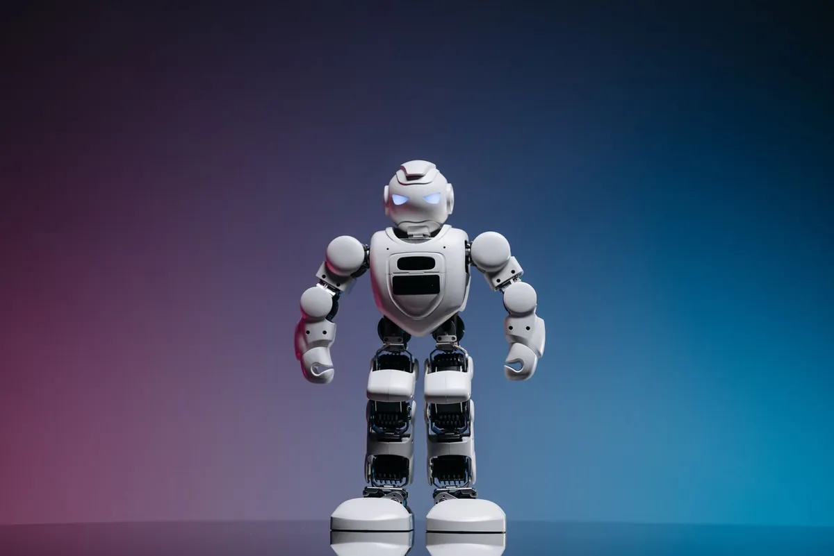 Small white humanoid robot standing on a pink and blue background
