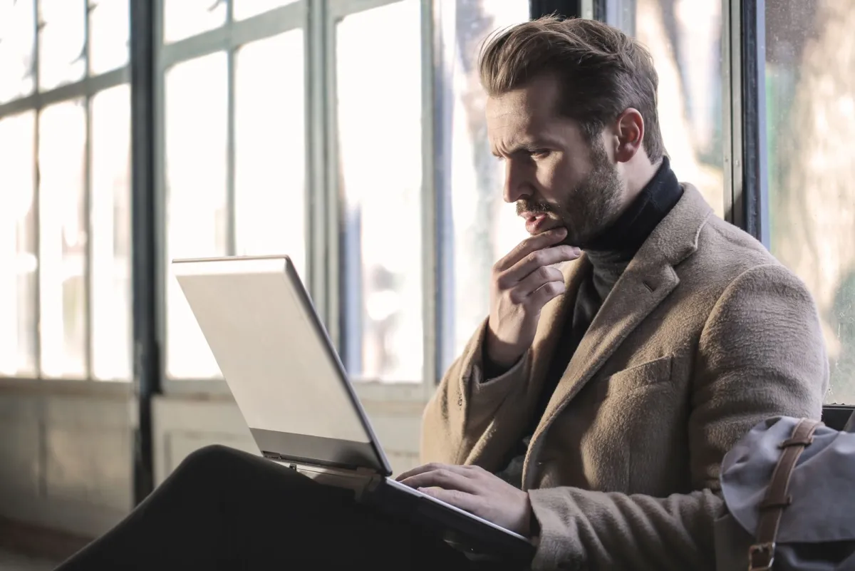 Man die een kop op zijn laptop herleest, met zijn kin in zijn hand